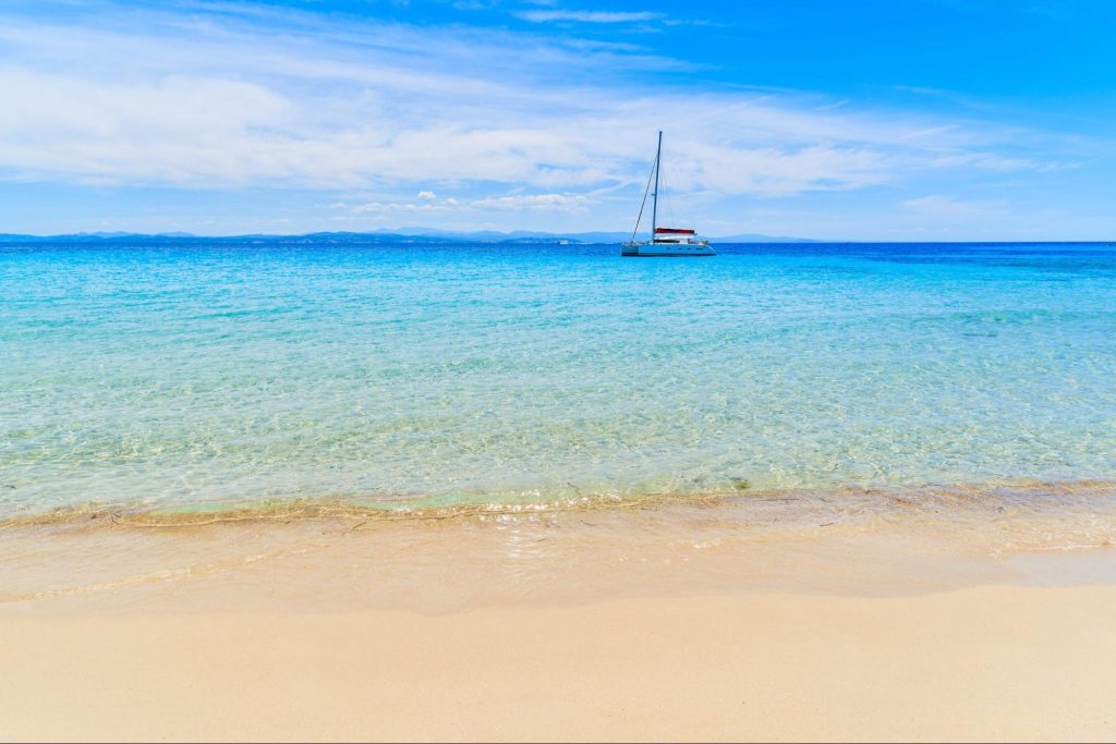 Helder turquoise water en zeilboot aan een strand op Corsica tijdens de beste reistijd voor een vakantie op het eiland