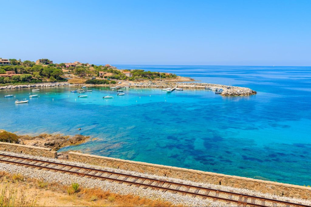 Trein langs de turquoise kust van Corsica met uitzicht op baaien en de Middellandse Zee.