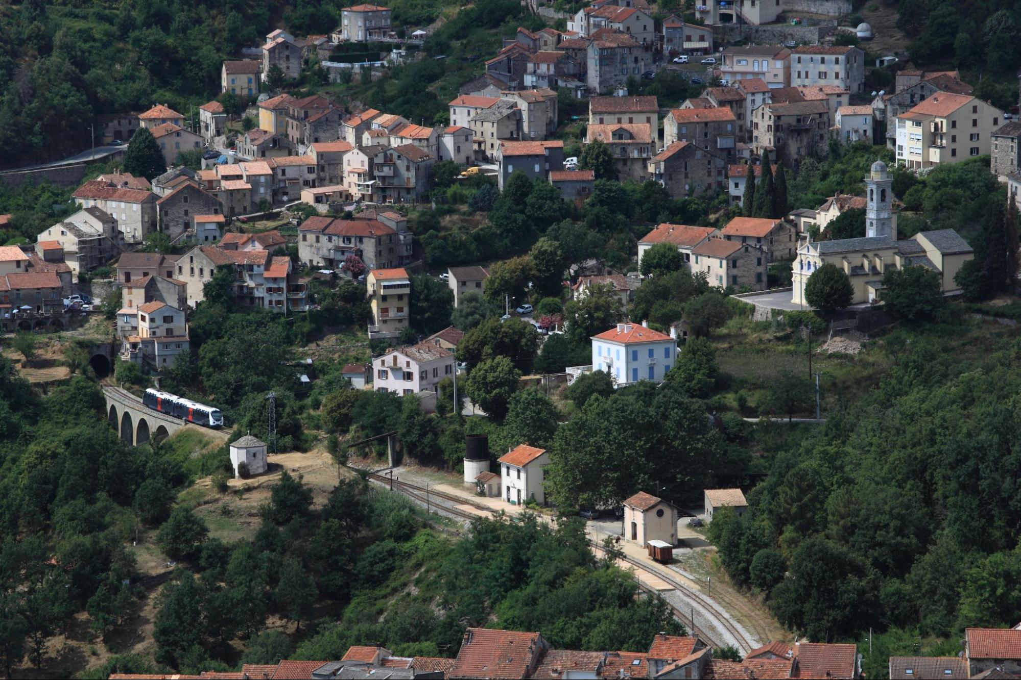 De Corsicaanse trein rijdt door een bergdorp met viaducten en groene heuvels in het binnenland.